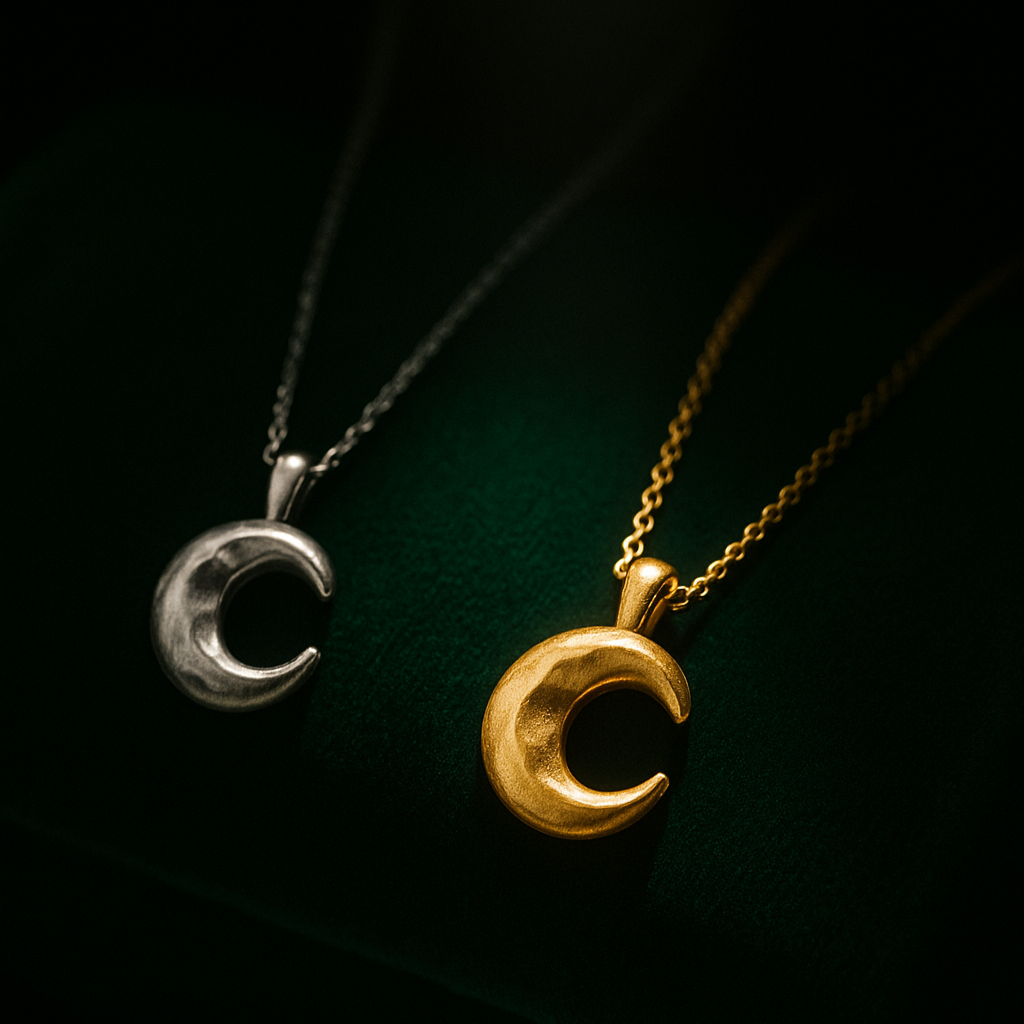 Two moon-shaped pendants, one gold and one silver, on dark green fabric.