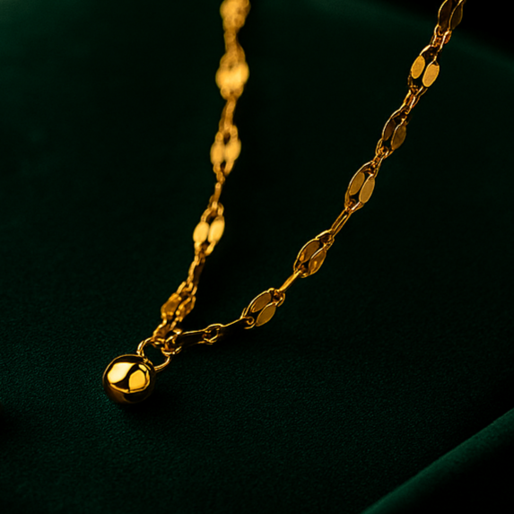 Two gold necklaces on a dark green surface with a black background