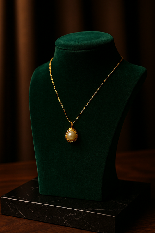 Gold necklace with a pendant on a green velvet bust against a dark background