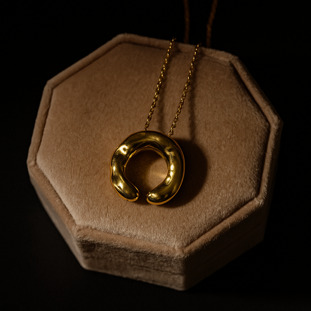 Gold necklace with a circular pendant on a brown hexagonal stand against a black background