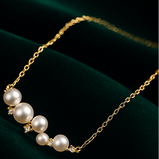 Two pearl necklaces, one silver and one gold, on a dark green fabric background.