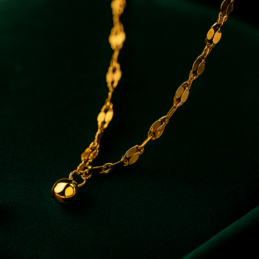 Two gold necklaces on a dark green surface with a black background