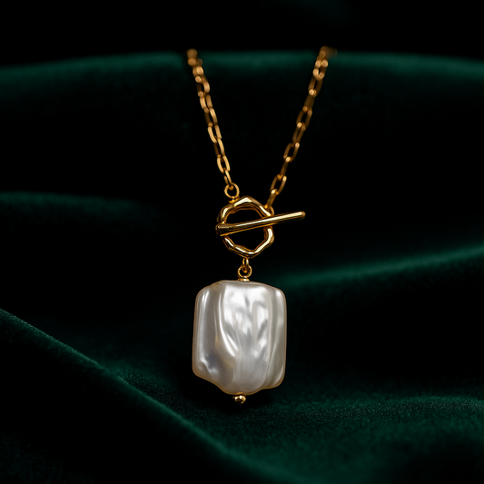 Gold necklace with a baroque pearl pendant on a dark green fabric background